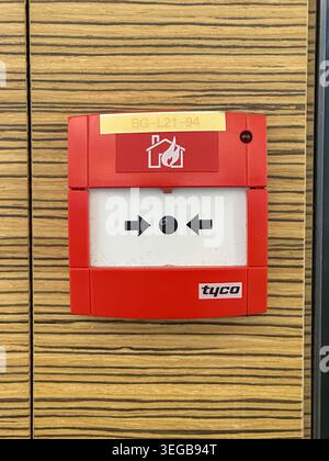 Johor, Malaysia, May 13, 2026: Red Tyco fire alarm call point mounted on wood‑patterned wall, showing arrows and flame safety icon. Stock Photo