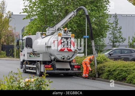 Leiden, Netherlands, May 08, 2026. A worker in orange high-visibility clothing operates a kolkenzuiger vacuum truck to clear a street drain. Stock Photo