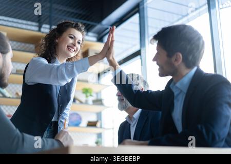 Business colleagues celebrating success in a boardroom. Two happy business people doing a high five during a meeting in an office. Teamwork and goal a Stock Photo