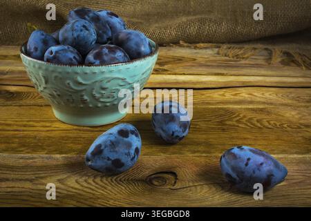 Fruit plums prunes in turquoise cup on old dark wooden background. Selective focus Stock Photo