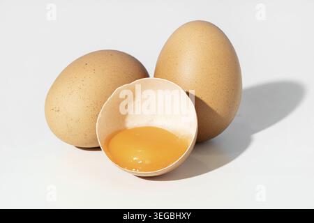 Studio shot of Two whole brown eggs and a broken eggshell containing an egg yolk isolated on white background Stock Photo