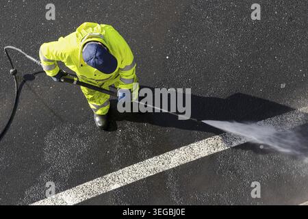 Road worker wearing high visibility clothing cleaning asphalt with high pressure water jet. High angle view Stock Photo
