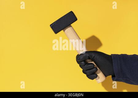 Construction worker holding a mason's hammer isolated on yellow background with copy space Stock Photo