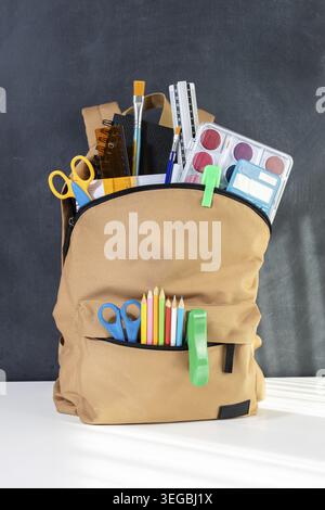 School backpack overflowing with Stationery Supplies on blackboard, ready for back to school season Stock Photo