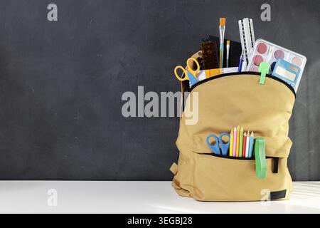 School backpack overflowing with Stationery Supplies on blackboard with copy space, ready for back to school season Stock Photo