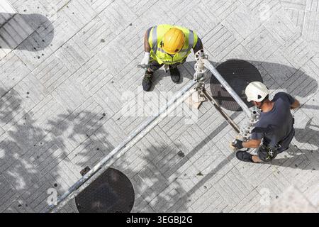 Aerial view of two construction workers assembling scaffolding on a city street sidewalk Stock Photo