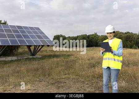 Happy Female Solar energy engineer or technician using a tablet to inspect a solar panel structure in a rural field Stock Photo