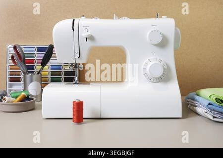 Modern sewing machine ready for tailoring projects alongside assorted colorful spools of thread and folded fabrics Stock Photo