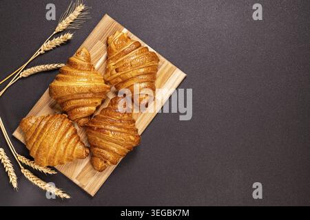 Golden, crispy croissants on a natural wood serving board, accompanied by wheat stalks, make for a tempting presentation of freshly baked European pas Stock Photo