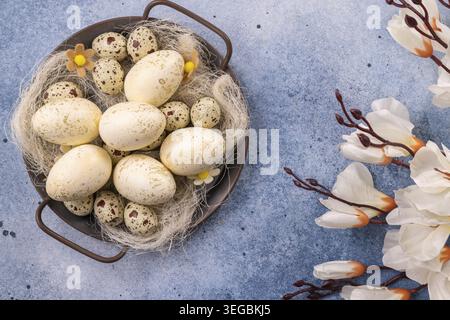 Speckled Easter eggs of various sizes are arranged in a rustic nest in a metal bowl that celebrates spring and holiday traditions. Delicate white flow Stock Photo