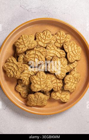 Maple leaf shaped cookies with cream filling that make a delicious snack or dessert option. They show a stack of cookies on an orange plate against a Stock Photo