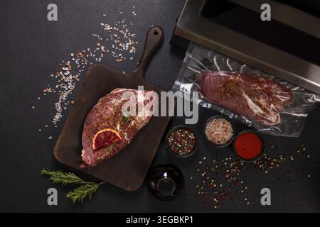 Raw meat, seasoned with herbs and spices, is prepared for vacuum sealing on a wooden board, with various spices such as salt and pepper shells spread Stock Photo