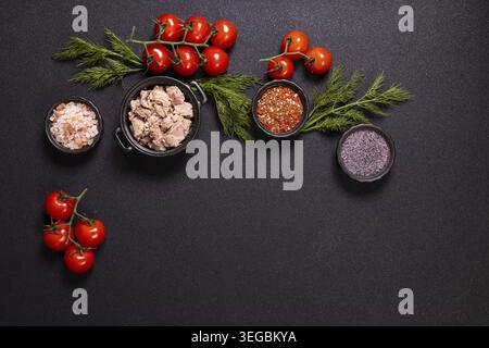 Fresh tuna pieces with ripe cherry tomatoes, dill, pink Himalayan salt, red chilli flakes and black poppy seeds on a dark background for Mediterranean Stock Photo