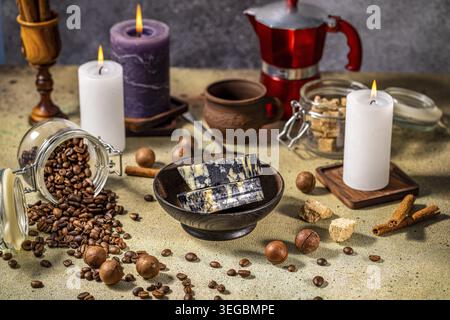 Marble cheese, coffee beans, macadamia nuts, burning candles, cinnamon sticks, brown sugar and coffee pot on a table create a cozy and inviting atmosp Stock Photo