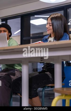 Diverse coworkers sitting at tall communal table in modern workspace, using laptop and notebook Stock Photo