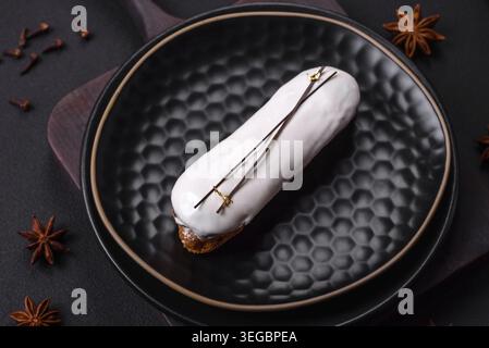 Food, Delicious fresh profiterole or eclair with chocolate on a black ceramic plate on a dark concrete background Stock Photo