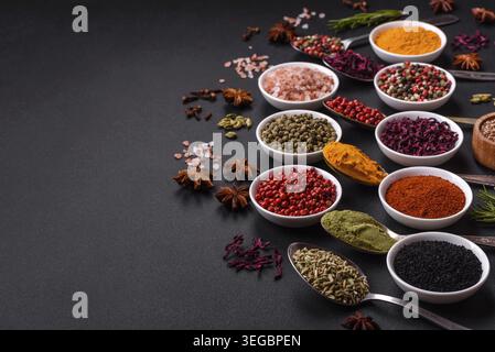 Food, Composition consisting of variations of spices in white bowls and metal spoons on a dark concrete background Stock Photo