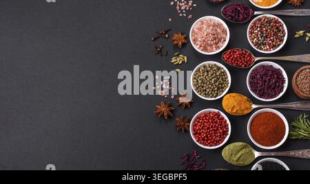 Food, Composition consisting of variations of spices in white bowls and metal spoons on a dark concrete background Stock Photo