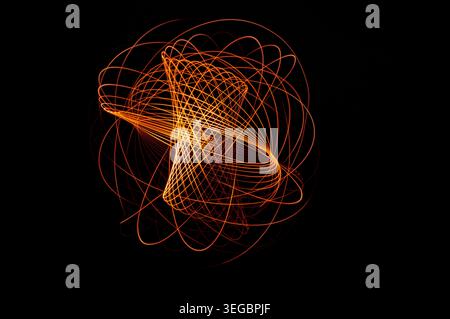 Abstract long exposure light painting featuring glowing orange and red light trails forming intricate geometric curves against a deep black background Stock Photo