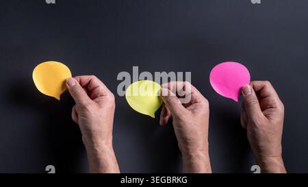 Close up of three Caucasian male hands holding blank colorful paper speech bubbles against a dark grey background with copy space Stock Photo