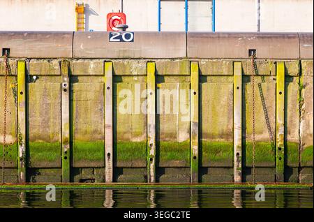 Concrete harbor quay wall with green moss algae and rusty chains at sea level in a port terminal Stock Photo