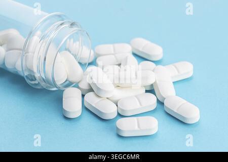 White medicine pills spilling from a container on blue background. Pharmacy concept Stock Photo