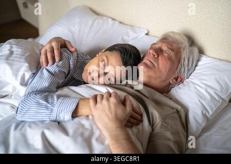 Positive senior couple husband and wife sleeping in bed together gently hugging with tenderness. Stock Photo