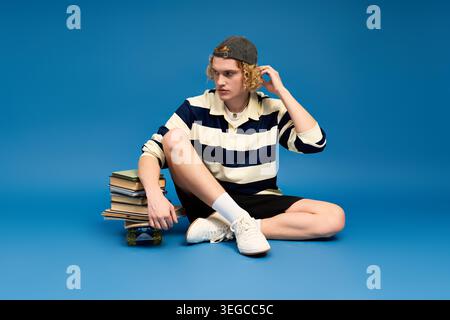 Curly haired student showcases unique fashion while relaxing on the studio floor with books. Stock Photo