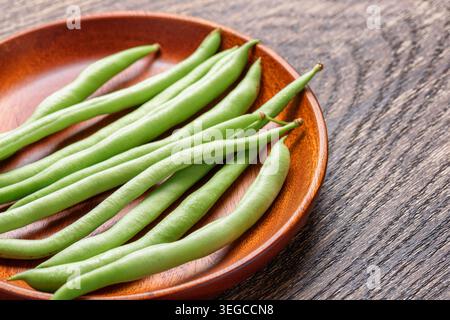 Closeup view of fresh green beans on wooden plate Stock Photo