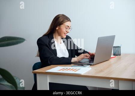 Attractive woman typing on laptop at office desk with documents. Business. Office work. Female professional focused on tasks. Beauty portrait. Corpora Stock Photo