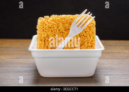 Dried instant noodles and white disposable fork in plastic plate Stock Photo