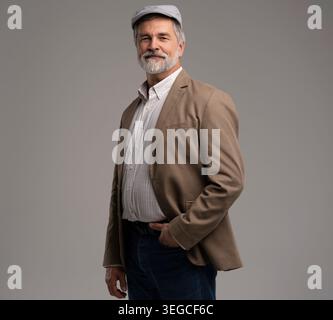 Attractive serious grey-haired man in suit and flat cap isolated on grey background Stock Photo