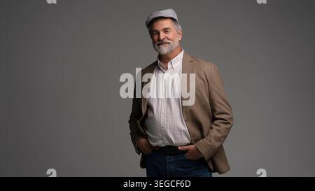 Attractive smiling grey-haired man in suit and flat cap isolated on grey background Stock Photo