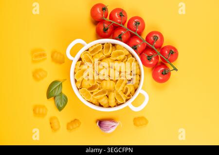 Uncooked sardinian malloreddus pasta in a white bowl with vine cherry tomatoes, fresh basil and garlic on a vibrant yellow background, essential itali Stock Photo