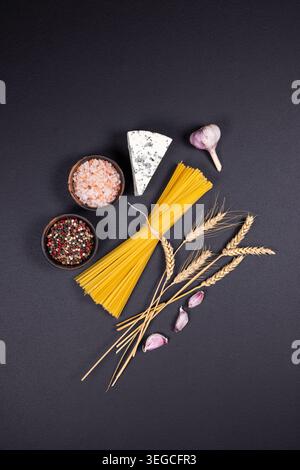 Spaghetti, wheat ears, blue cheese, garlic, salt, and peppercorns artfully arranged on a dark background, representing traditional italian cooking ess Stock Photo