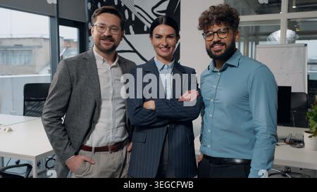 Three multiethnic business workers in office smiling happy friendly posing looking at camera corporate team diversity colleagues standing indoors Stock Photo