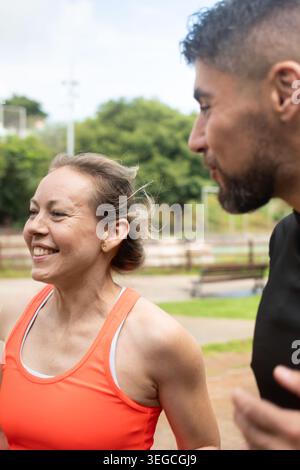 Active man and woman enjoying a conversation while jogging outdoors in a tropical park. Healthy lifestyle, fitness motivation and wellness concept wit Stock Photo