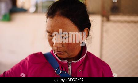 Asian woman looking down, wearing a pink jacket, contemplating outdoors Stock Photo