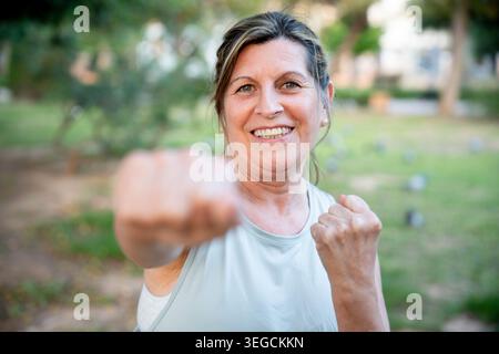 Senior woman smiling and punching, training boxing outdoors, symbolizing active lifestyle, strength, and empowerment Stock Photo