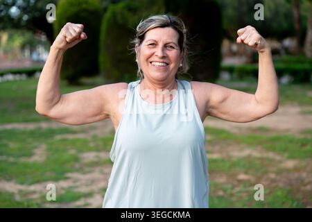 Senior woman flexing her biceps, symbolizing strength and active healthy aging. Happy and confident, she embraces fitness outdoors Stock Photo