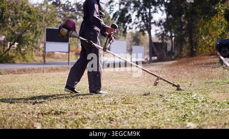 Worker trimming overgrown grass and weeds using a gas powered brush cutter Stock Photo