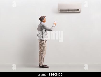 Elderly man standing and using a remote control to adjust a wall-mounted air conditioner Stock Photo