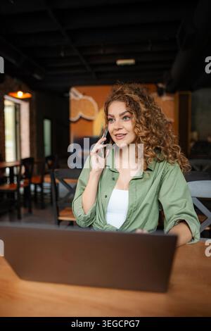 Freelancer working remotely from cafe, talking on phone and using laptop Stock Photo