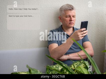 A man sitting on a sofa while looking at a smartphone, engaging with AI tool Stock Photo