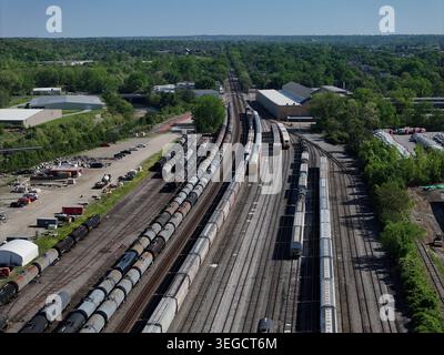 Aerial view of freight trains parked on multiple tracks in a railway yard surrounded by lush green trees and industrial buildings Cincinnati, OH, Unit Stock Photo