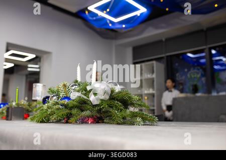 A beautiful Christmas evergreen arrangement with candles and ornaments on a restaurant table with waiters standing in the background. Stock Photo