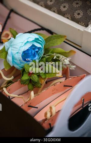 Beautiful light blue artificial peony with fresh green leaves and silver ribbon placed on top of neatly arranged pink gift boxes tied with black twist Stock Photo
