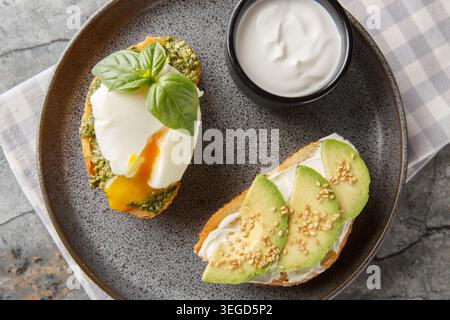 healthy snack of toast with a poached egg and basil pesto, along with avocado and cream cheese, served with sour cream, close-up on a plate on a table Stock Photo