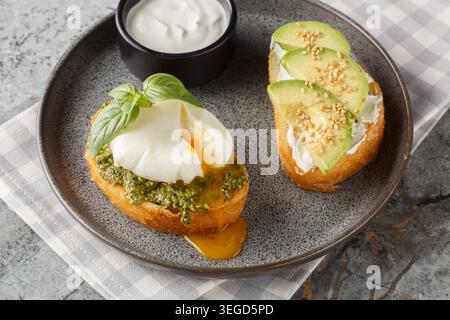 Keto breakfast toast with poached egg and basil pesto, avocado, and cream cheese, close-up on a plate on a table. Horizontal Stock Photo