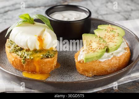 Low-carb toast with poached egg and basil pesto, as well as with avocado and cream cheese close-up on a plate on a table. Horizontal Stock Photo